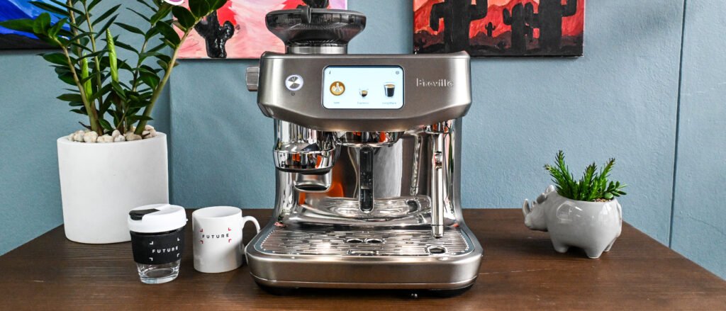 A wide front-on view of the Breville Oracle Jet coffee machine sitting on a dark wooden table with decorative plants to either side.