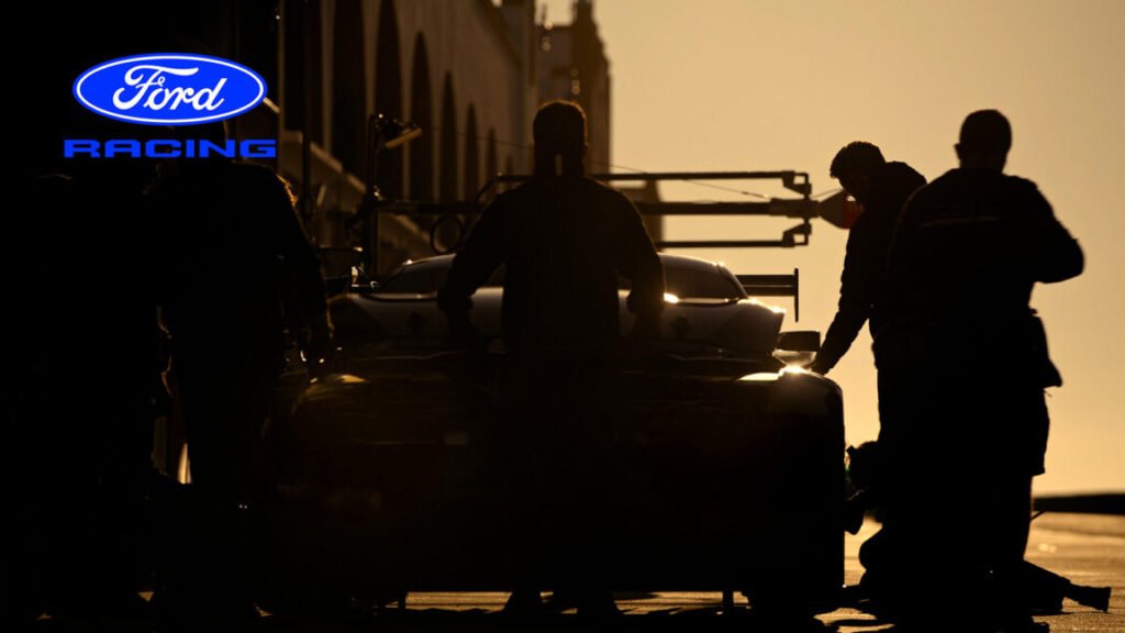 A moody photograph of a race car in the pit lane, but the car and the people are all in shadow