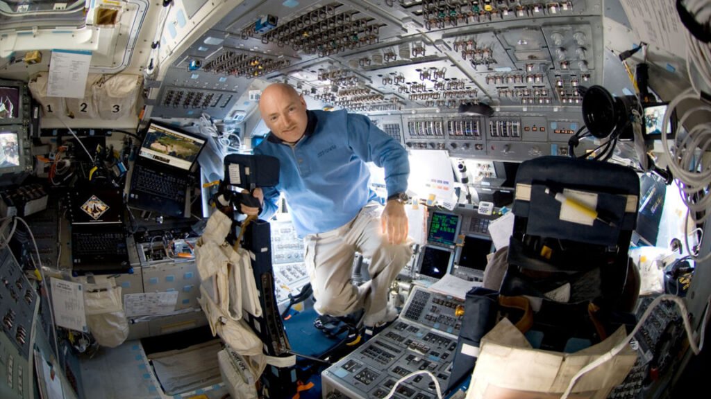 a man in a blue shirt and khaki slacks is seen surrounded by switches and displays aboard a spacecraft