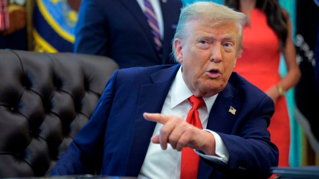 President Donald Trump sits at his desk and talks while pointing a finger.