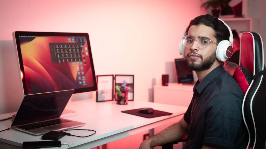 Man with headphones sitting at a desk with a laptop and monitor recording