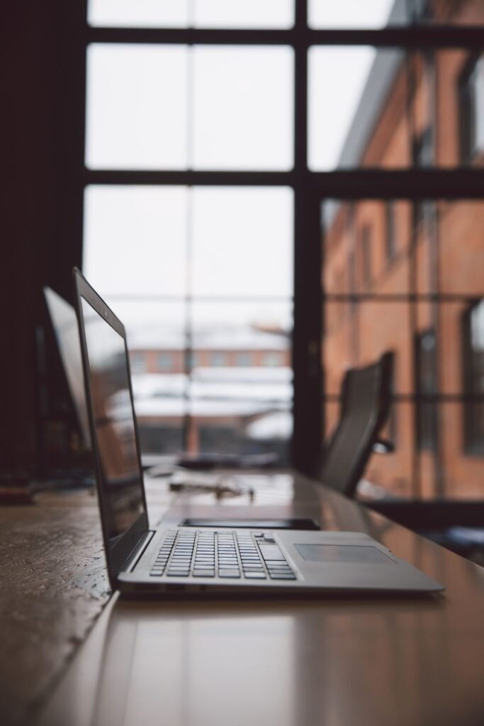 Windows 11 vs Windows 10: Should You Upgrade? A laptop computer on a wooden desk in front of large windows with natural light