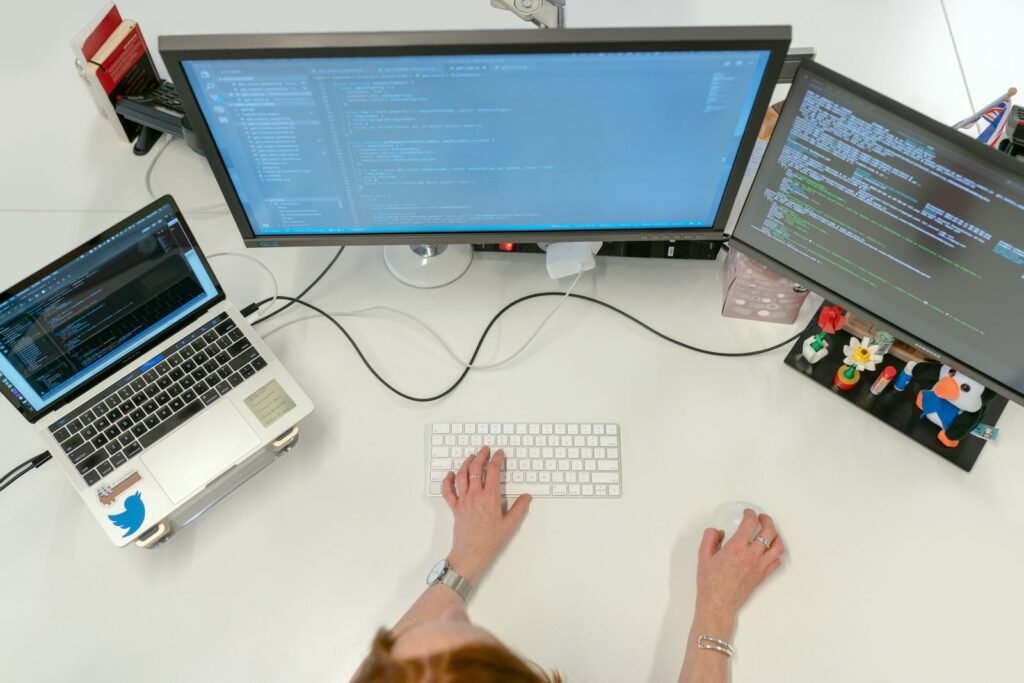 Woman analyzing code and security data across dual monitors in a modern office, representing non-traditional entrants to cybersecurity careers