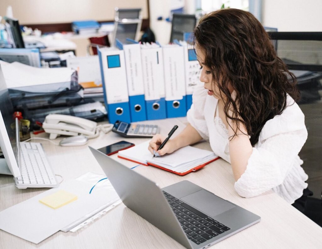 How to Use Microsoft Word for Beginners Woman writing on a notebook while using a laptop