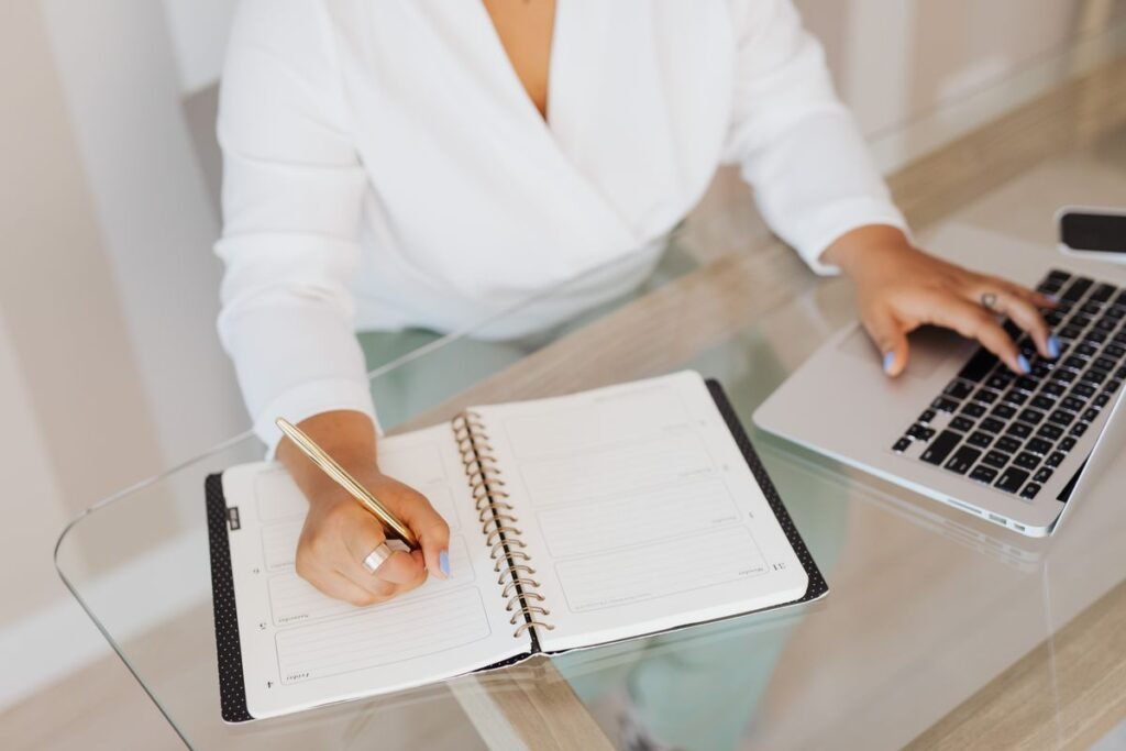 Person writing on a notebook while using a laptop
