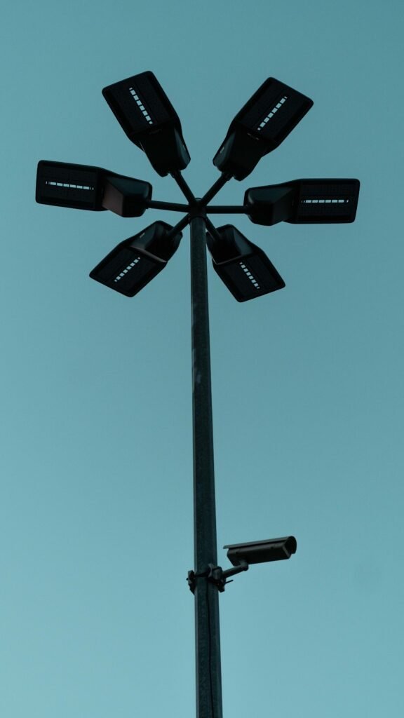 A surveillance camera mounted on a streetlight against a blue sky, illustrating the AI object detection systems the Digital Camouflage shirt is designed to confuse