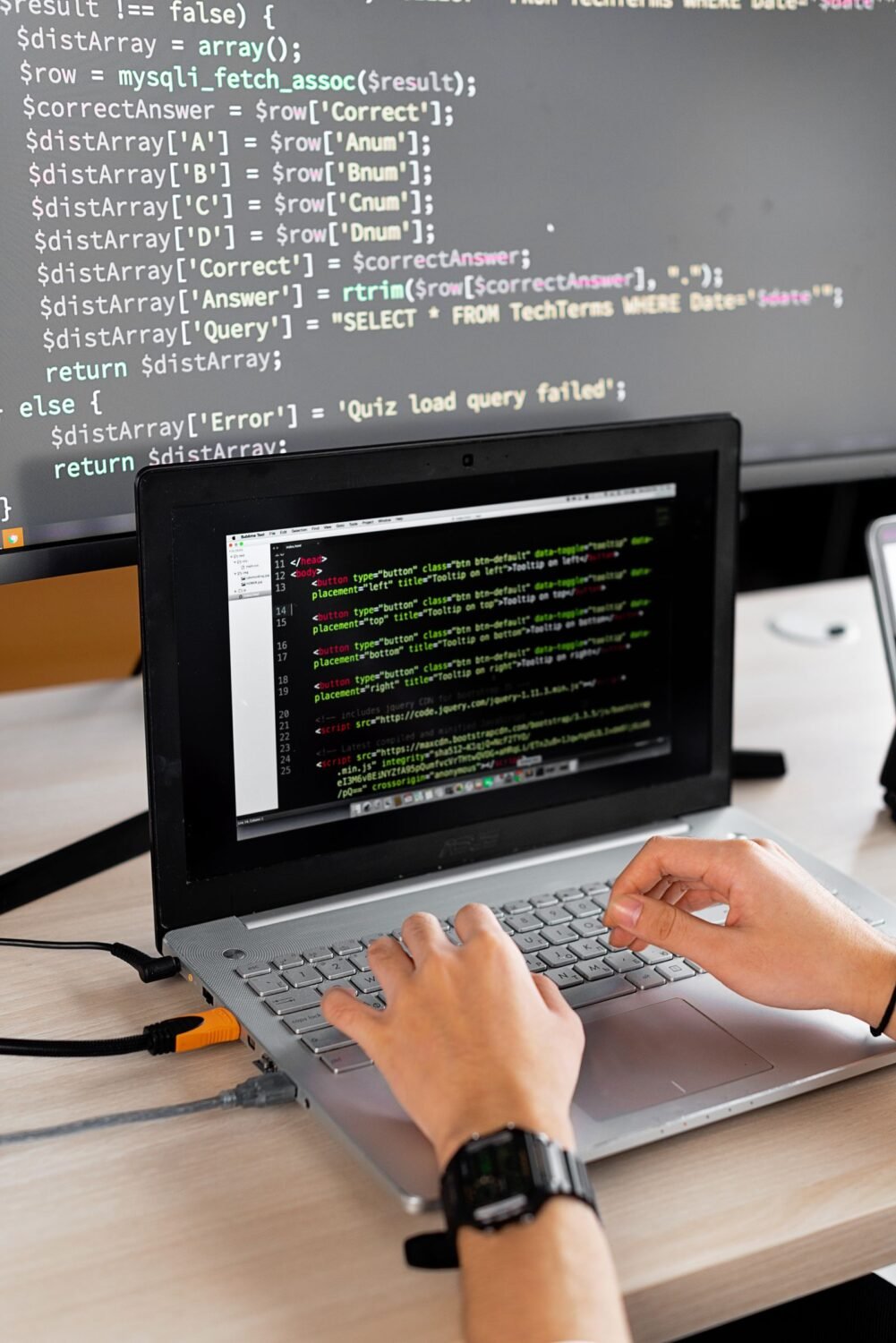 A developer writing code at a desk with a laptop and external monitor