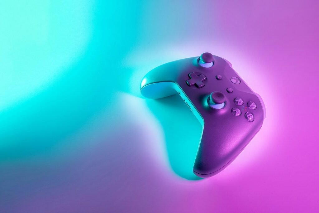 A wireless game controller lit by cyan and magenta neon light on a dark surface