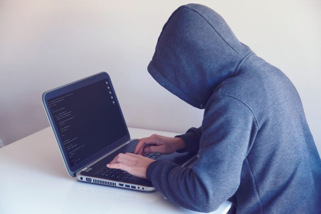 A hooded figure working on a laptop, representing infostealer malware and account hijacking