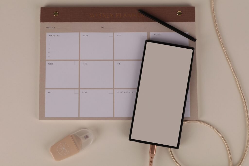 A flat lay desk setup with a weekly planner, a smartphone and stationery