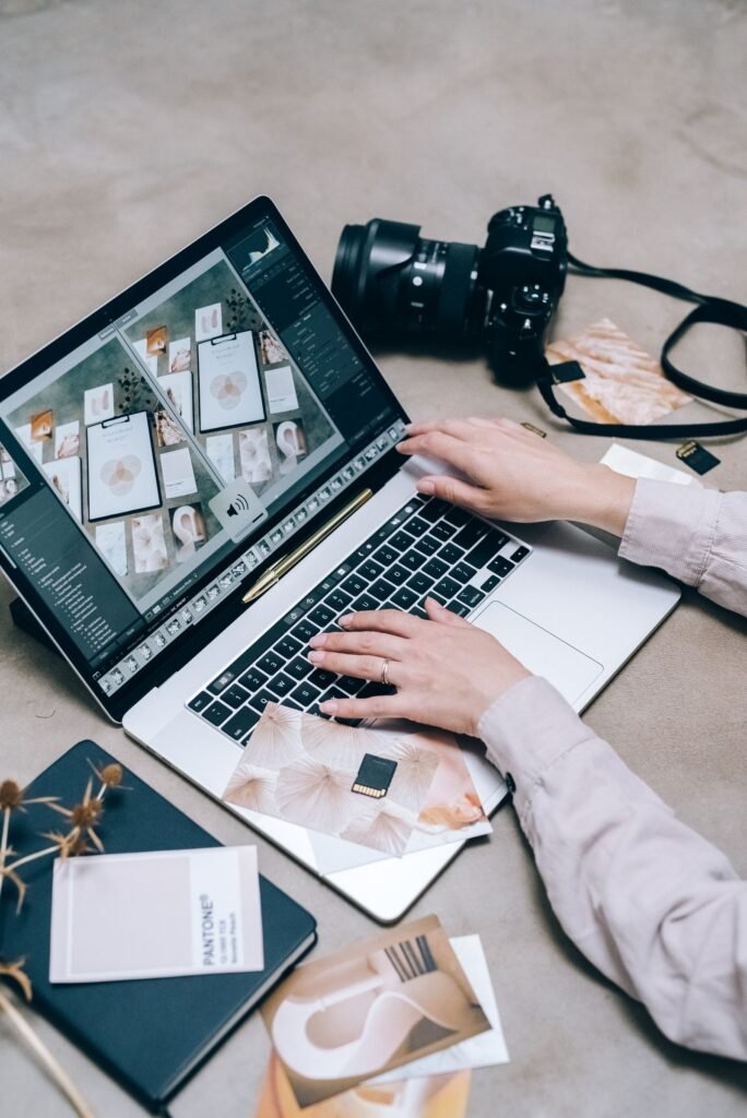 Hands editing photos on a laptop with a camera lying on the desk beside it