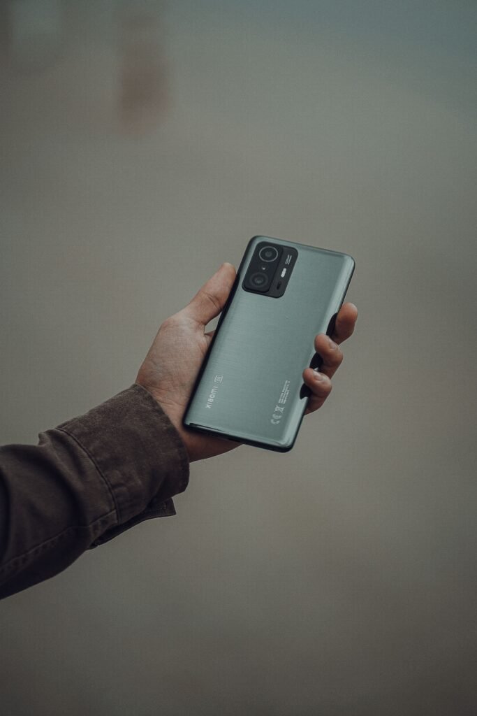 A hand holding a modern smartphone against a plain grey background