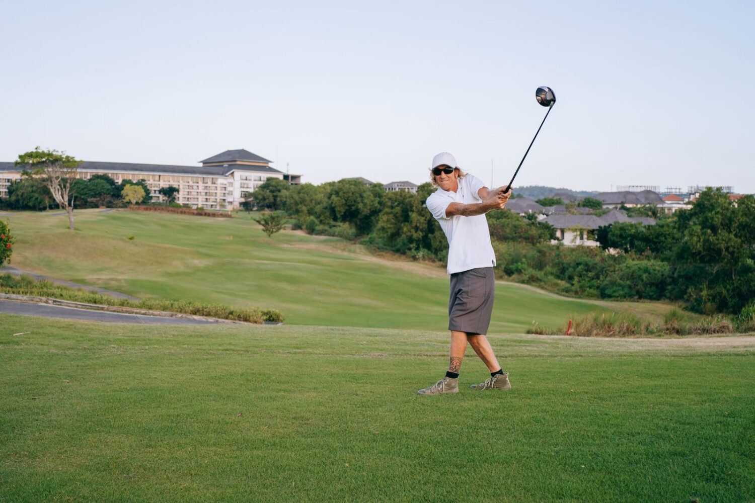A golfer mid-swing on a green golf course on a sunny day