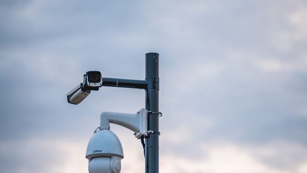 Hackers Pulled a Flock Camera Off a Pole. The Encryption Key Was Sitting Inside It. Security cameras mounted on a pole under a cloudy sky
