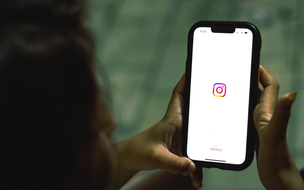 Hand holding a smartphone with the Instagram icon on screen for linking Instagram to a Facebook Page
