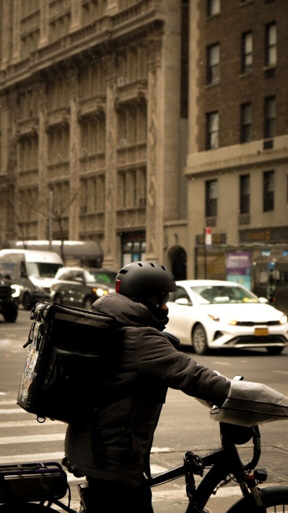 A food delivery courier on a bike with an insulated bag, illustrating the DoorDash $131.5 million settlement with New York City over Dasher pay