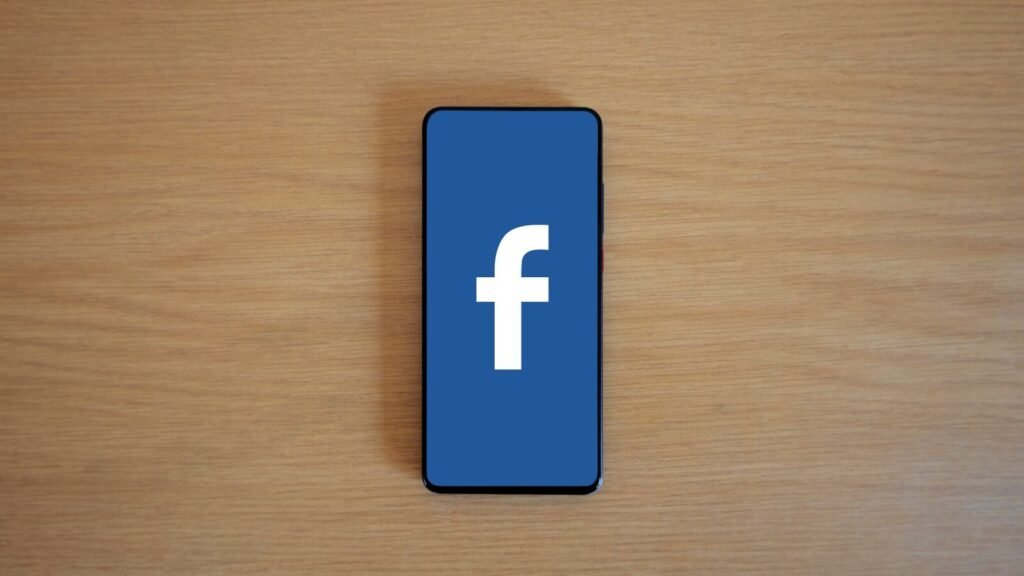 How to Create a Facebook Cover Photo (Sizes and Tips) Smartphone with the Facebook logo on a wooden surface