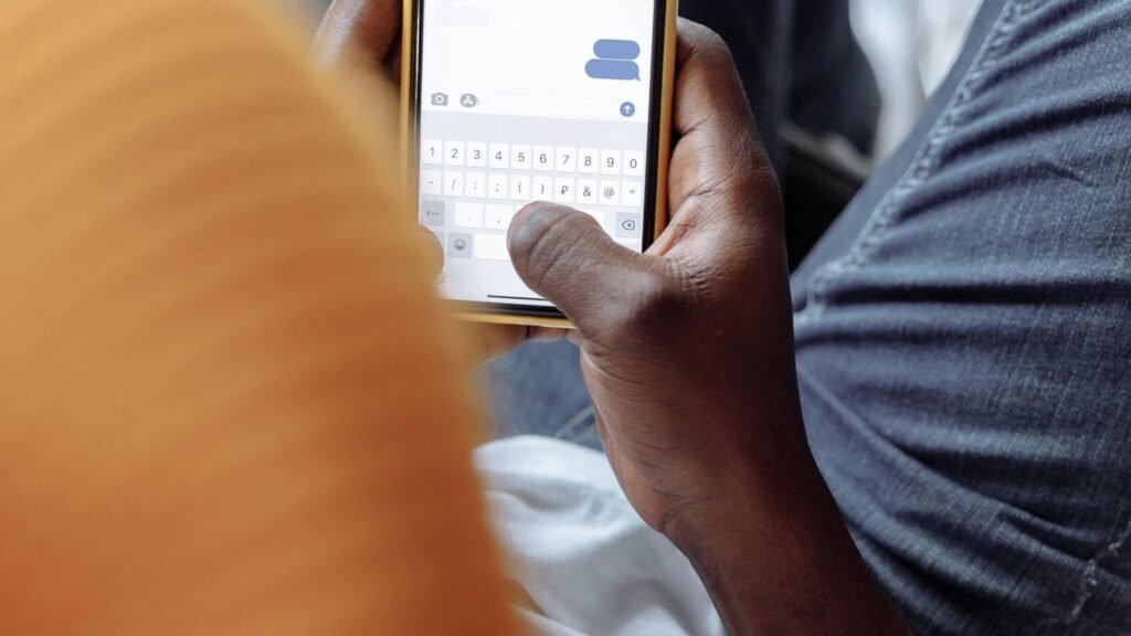 Google Messages Copied iMessage Backgrounds. It Fixed the Part Apple Got Wrong. A person texting on a smartphone, illustrating custom chat themes and backgrounds in Google Messages