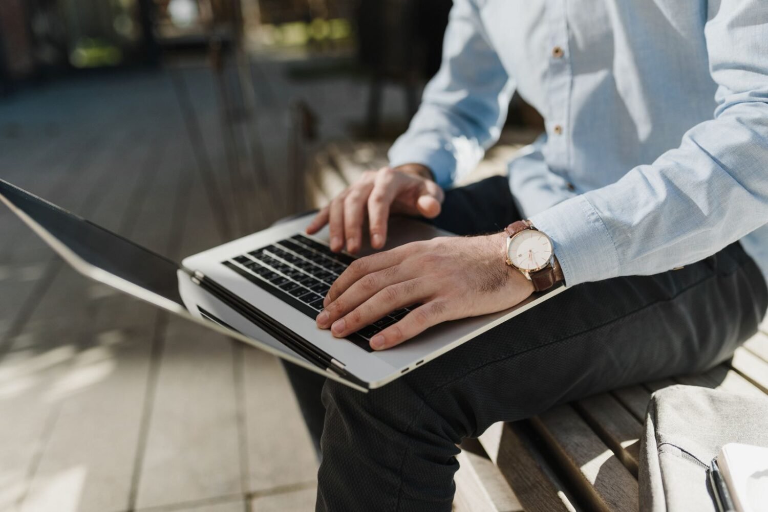 Close-up of a person wearing an analog-style hybrid smartwatch while typing on a laptop