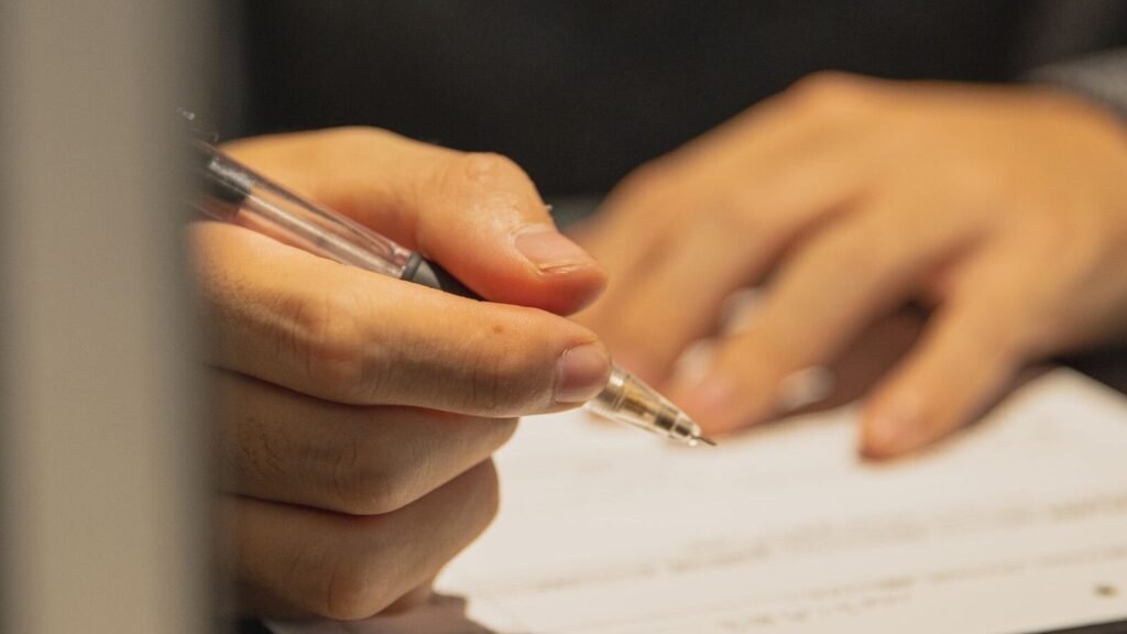 Person filling out a paper form with a pen at a table