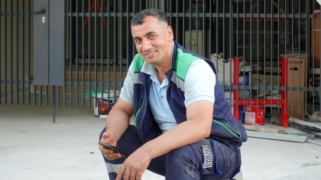 Outdoor worker in a hard hat checking a smartphone, illustrating the field use case for a rugged phone with a 16,000mAh battery