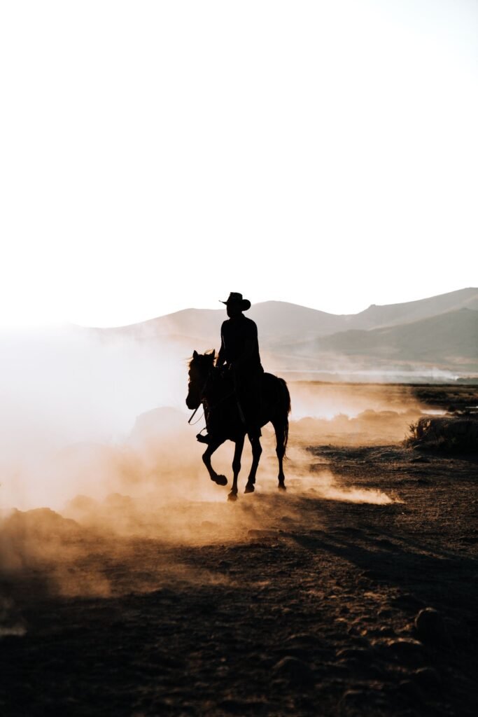 Lone rider silhouetted against dawn light on a dusty plain, evoking Sadie Adler's bounty hunting years in Red Dead Redemption 2