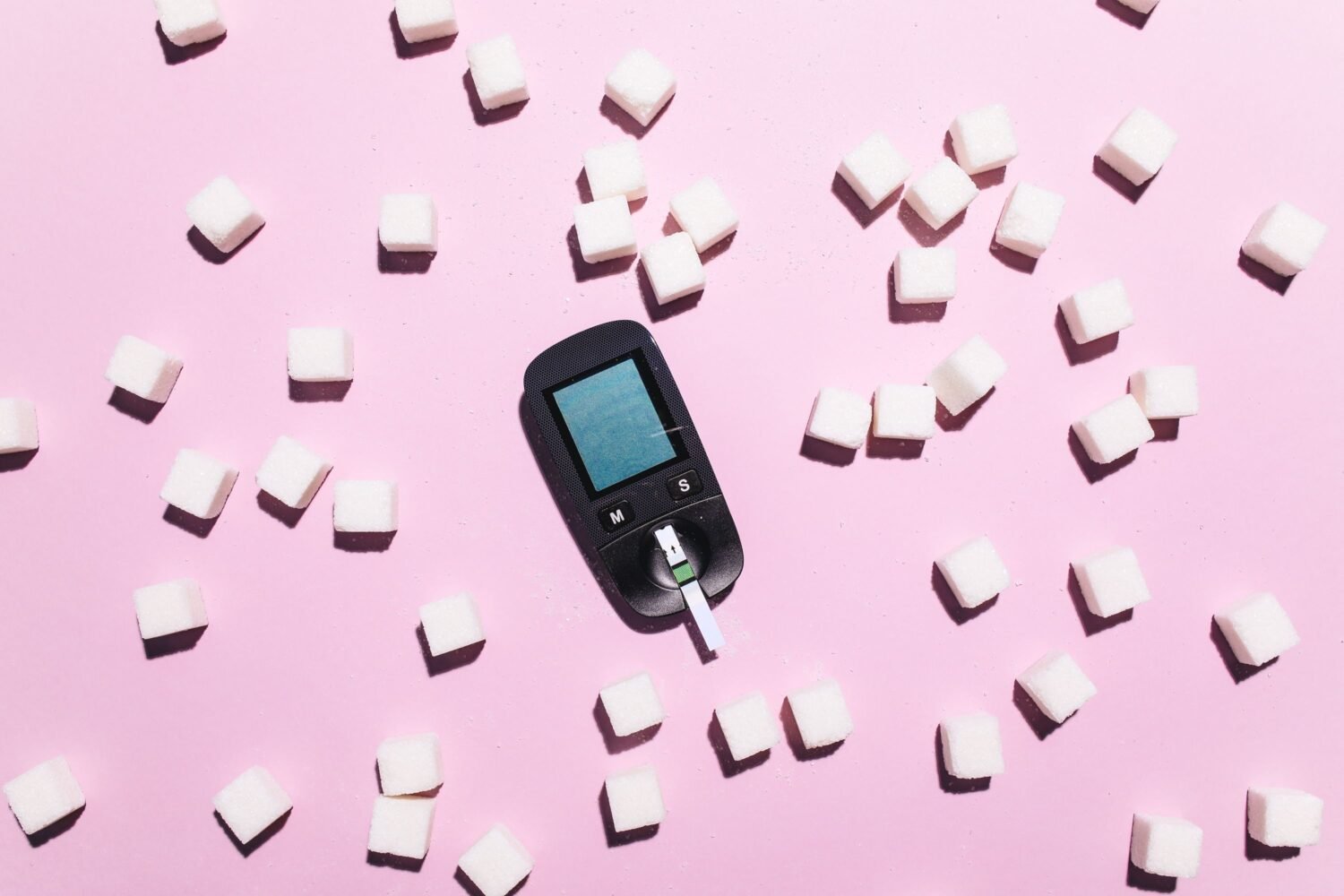 Blood glucose meter and test strip next to sugar cubes, representing glucose monitoring