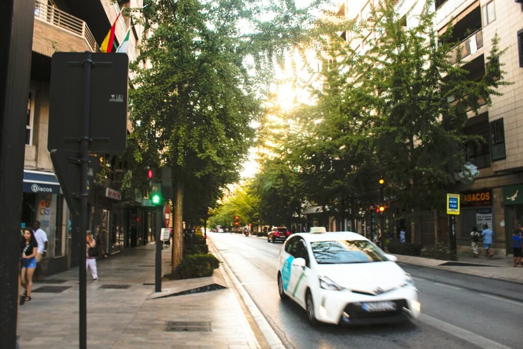 A white taxi on a tree-lined city street, illustrating the Tesla Cybercab robotaxi launch in Austin