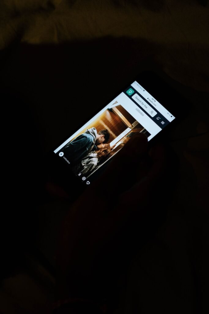 Person holding a smartphone in a dark room, screen lighting up their hands