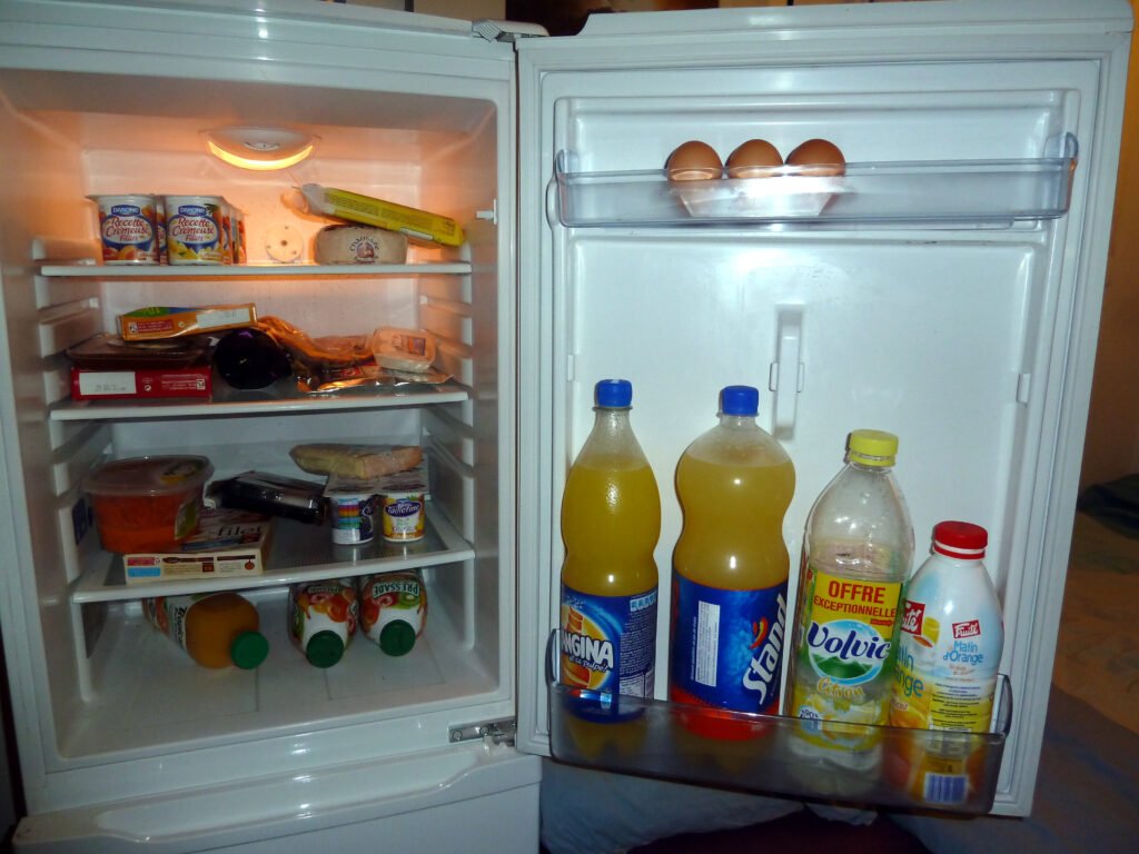 Hands placing food containers onto the shelves of an open refrigerator
