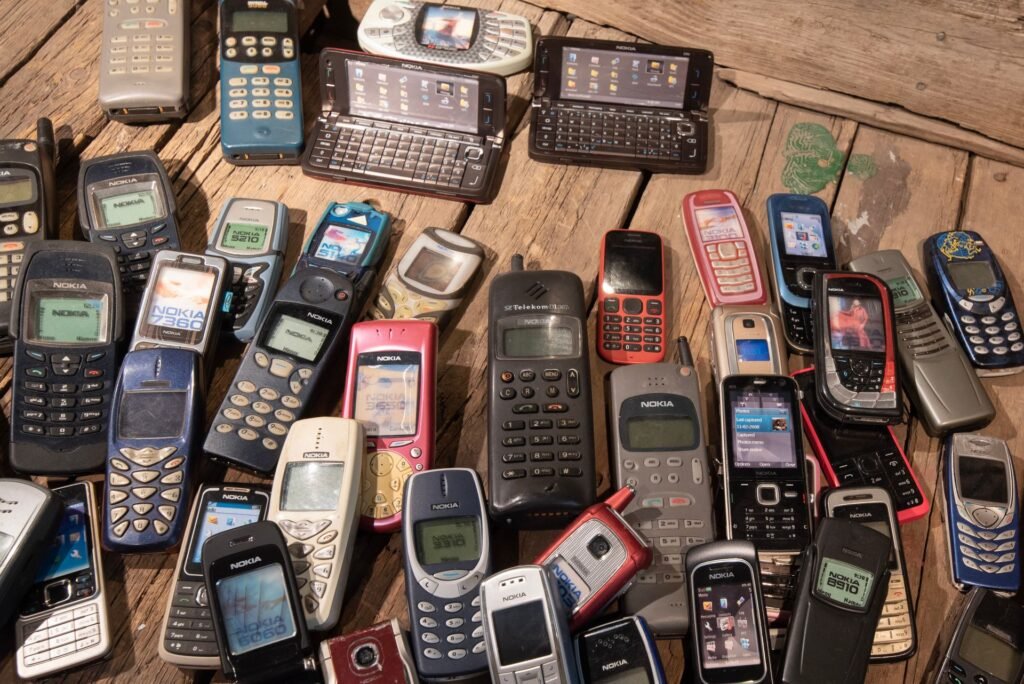 A pile of old Nokia and other keypad mobile phones from the 2000s on a wooden table