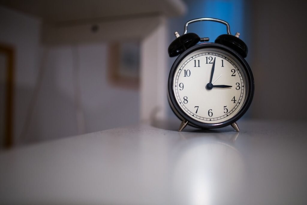 Classic black alarm clock with a white face showing 7:05, the kind of clock you still have to set back by hand