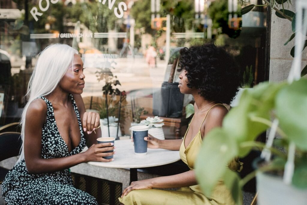 Two women having a conversation at a coffee shop table, the kind of chat an AI wearable like Amazon Bee Frontier could transcribe