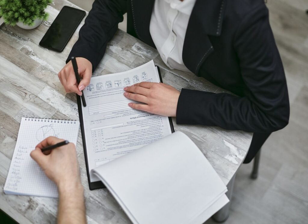 Anthropic Is Putting Outside Auditors on Its Payroll Laptops, and Giving Up the Veto Two colleagues reviewing documents together at a desk, illustrating independent auditors working inside Anthropic