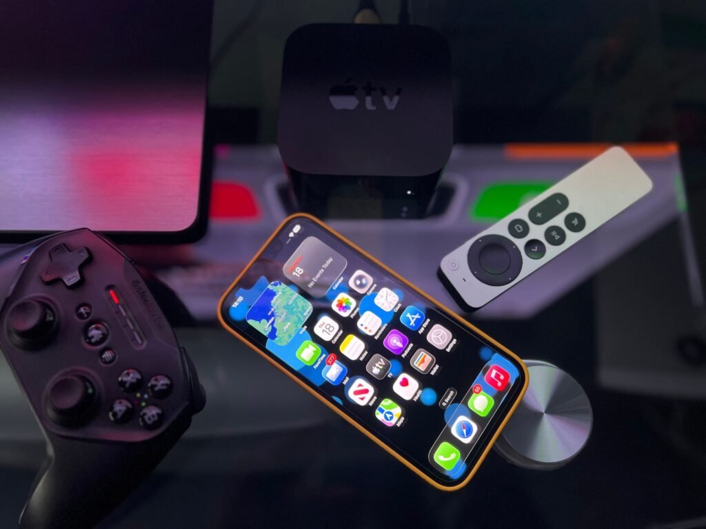 Apple’s New $299 Apple TV Gets Siri AI. So Does the One You Already Own. Apple TV box next to an iPhone and a game controller on a dark surface
