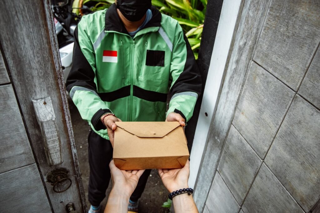 A delivery courier handing a cardboard package to a customer standing in a doorway