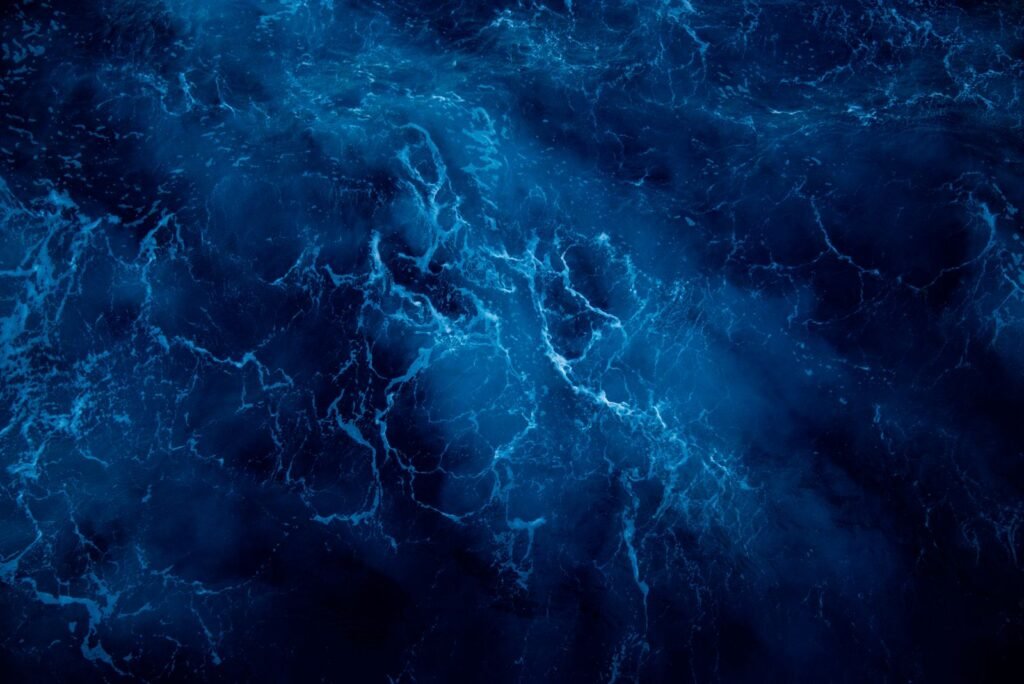 Aerial top down view of deep blue ocean water with white foam patterns on the surface