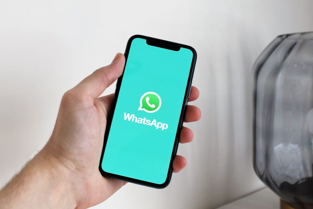 A hand holding a smartphone with the green WhatsApp logo on the screen
