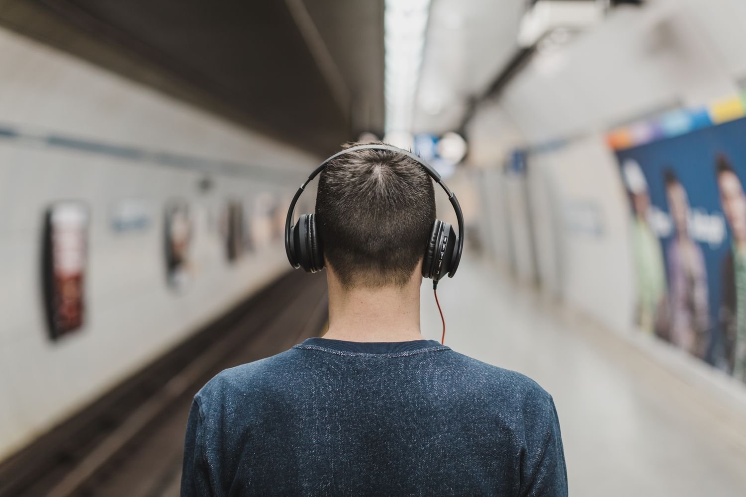 Man wearing over ear headphones walking along an underground subway platform