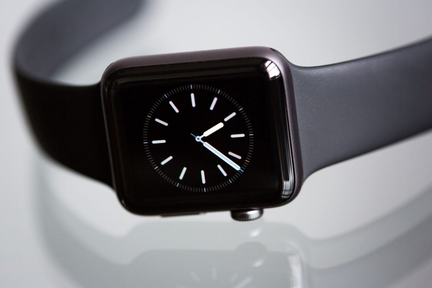 Black smartwatch with an analog-style watch face resting on a glossy surface