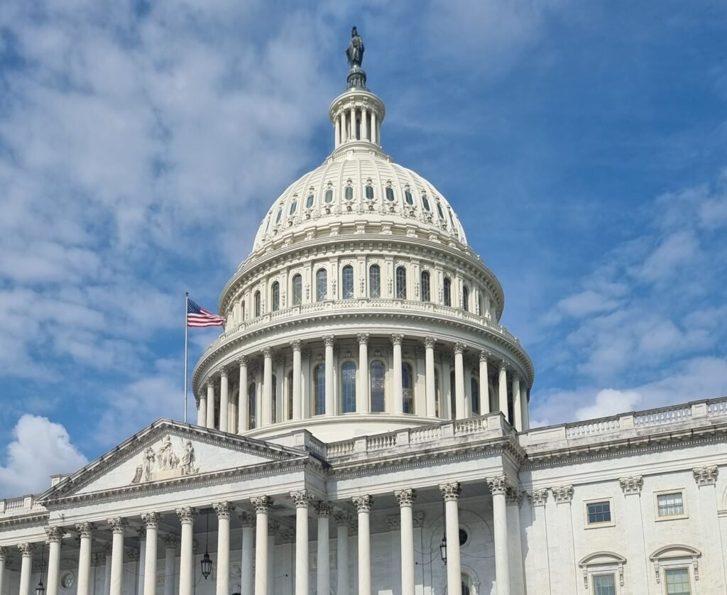 The United States Capitol dome and flag under a blue sky in Washington, DC