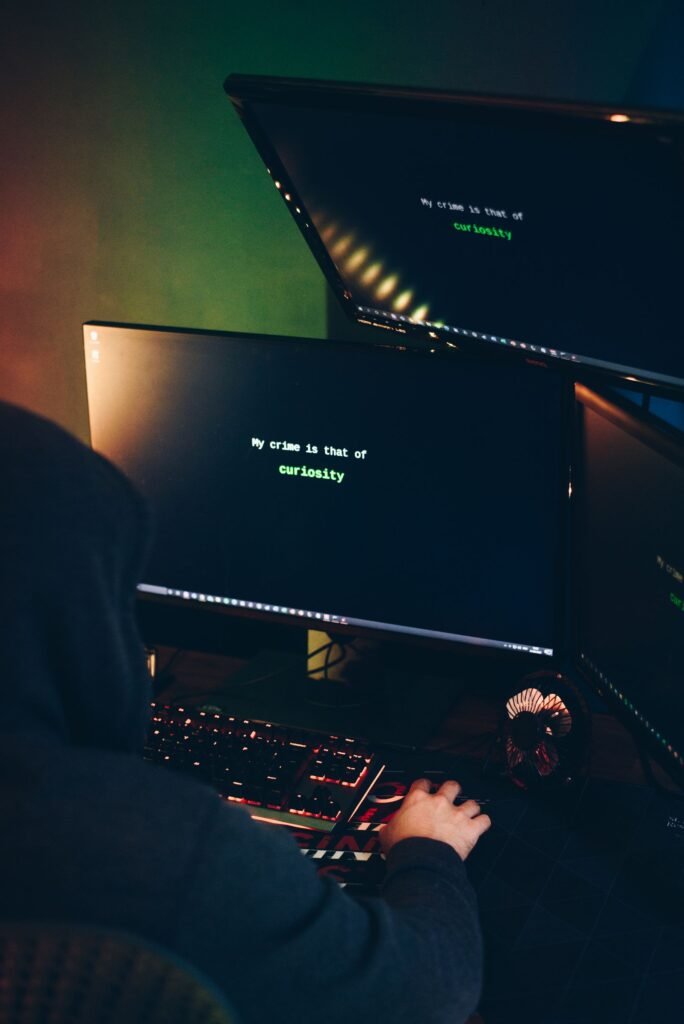 Person monitoring multiple computer screens in a dark room, illustrating cybersecurity oversight