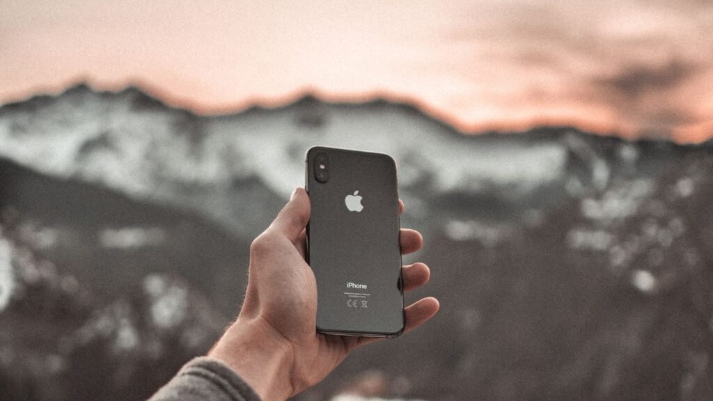 Verizon’s CEO Says Starlink Can’t Compete. You Can Already Put It on a Verizon Phone for $10. Hand holding a smartphone in front of snowy mountains far from cell towers