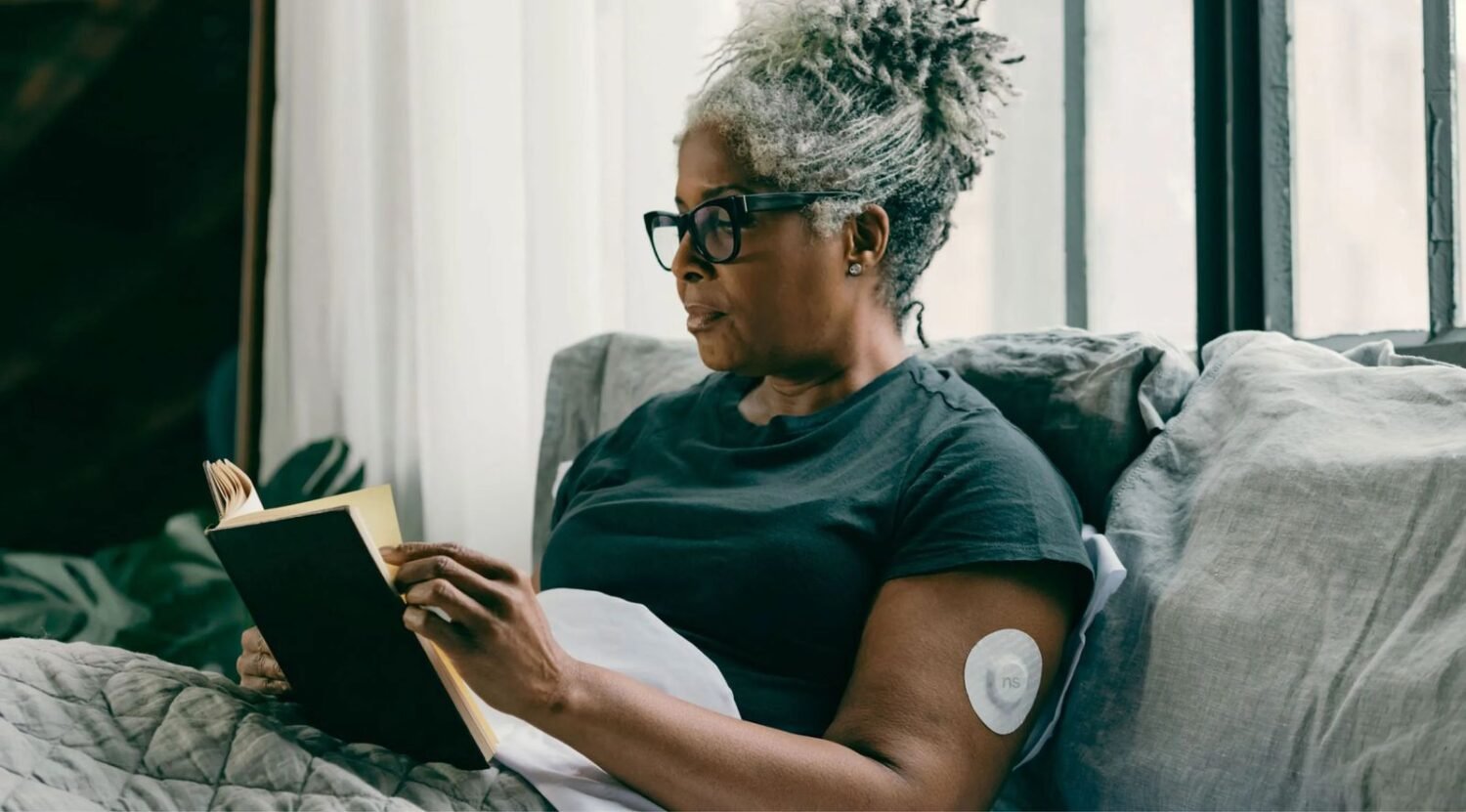 Woman with diabetes wearing a continuous glucose monitor sensor on her upper arm while reading a book