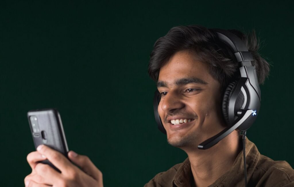 A smiling young man wearing a gaming headset with a microphone while looking at his smartphone