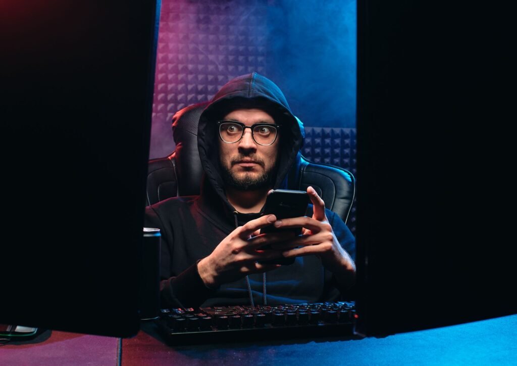 Man in a dark hoodie holding a smartphone in a dimly lit room, illustrating the Trump Mobile customer data leak