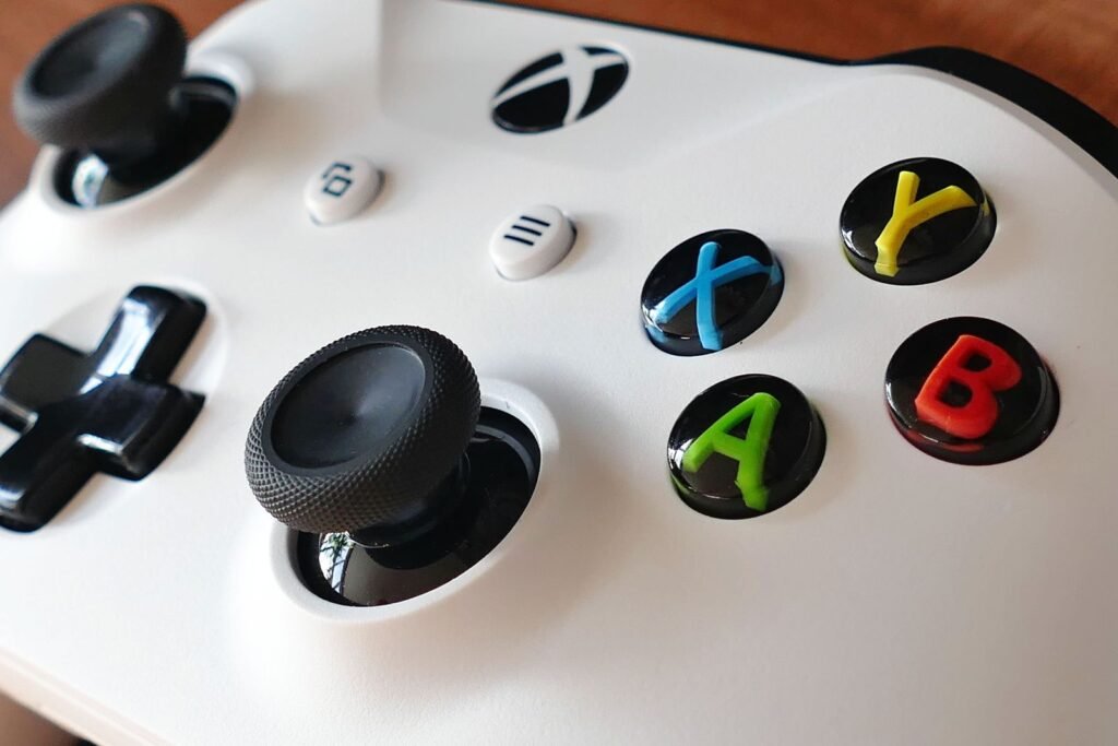Close up of a white Xbox controller showing the left thumbstick, D pad and colored ABXY buttons